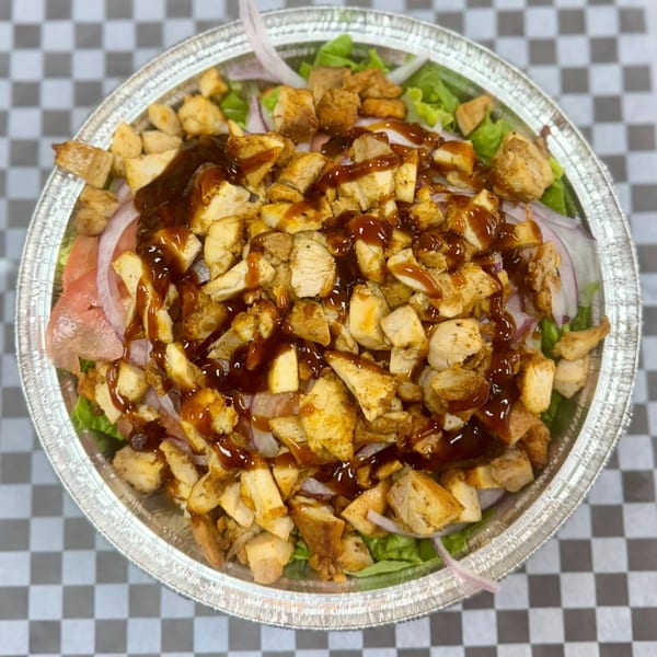 Halal chicken and rice platter with sauce, lettuce, and onions in a foil container.