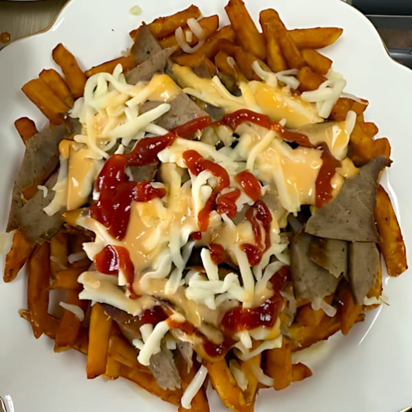 A plate of golden fries topped with gyro meat, melted cheese, and a drizzle of ketchup and sauce.