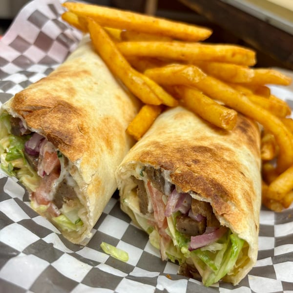 Two halal gyros with meat, lettuce, onions, and sauce, served with a side of golden french fries.