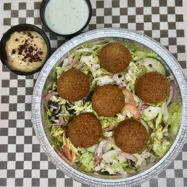 A falafel salad with hummus and tzatziki sauce on a checkered background from Reunion Gyro Halal Restaurant.